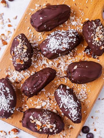 Nine chocolate covered dates on a wooden serving board.