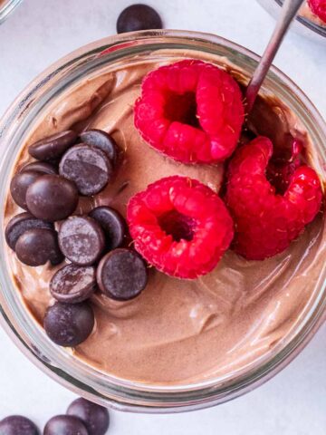 A pot of chocolate yogurt topped with raspberries and chocolate chips.