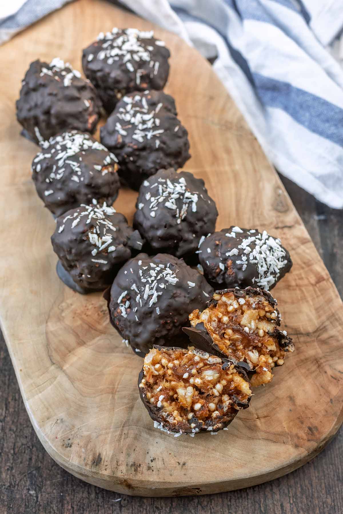 Nine chocolate covered date balls on a wooden serving board.